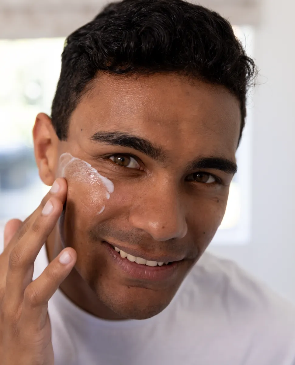 happy biracial man applying face cream in bathroom utc