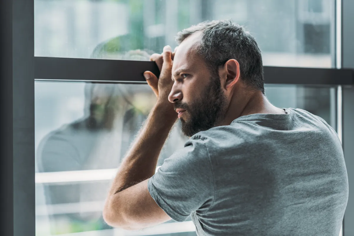 upset bearded man leaning at window and looking th utc